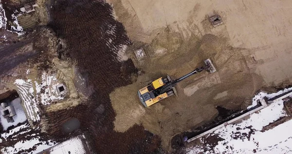 Uma escavadeira industrial em uma seção de estrada aberta carrega rocha e terra em um caminhão de descarga muito grande, carregado com minério. O balde da escavadeira goteja e carrega o minério. Panorama de obras de construção. — Fotografia de Stock
