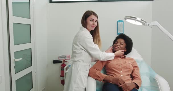 Kvinnlig patient afroamerikan på sjukhus mottagning sitter i Cosmetologists stol. Förbereda flicka för mesoterapi förfarande Kosmetolog kommunicerar med patienten. Hudvård och hudvård. — Stockvideo