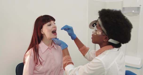Concept van behandeling en preventie van keelziekten. Een Otolaryngoloog onderzoekt een vrouwelijke keel met een houten spatel. Een mogelijke diagnose is de ontsteking van de farynx tongen of faryngitis — Stockvideo