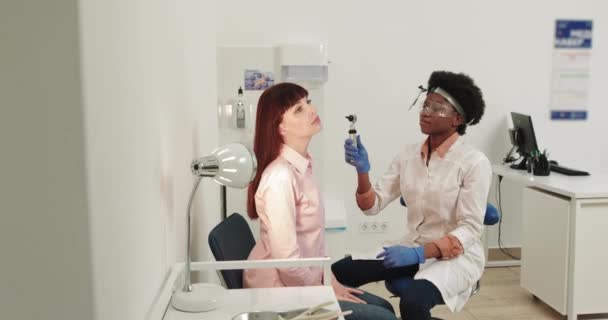 Läkare ENT. Kvinnlig afroamerikansk doktor. En Otolaryngolog undersöker örat på en flicka som klagar på smärta. Smärtlindring och behandlingskoncept. Inflammation i hörselgången eller trumhinnan. — Stockvideo