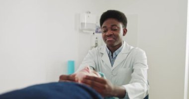 Afro-Amerikalı masöz doktor. Kadın yüz masajı yaptırıyor. Fizyoterapist, Modern Rehabilitasyon Kliniğindeki Kas Gücünü Yenilemek İçin Genç Bir Kadın 'a Terapi Yapıyor