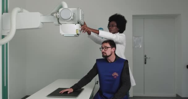 Röntgen a férfi kézről. Az afro-amerikai orvos modern kézröntgent készít. A női technikus beállítja a röntgengépet az orvosi szekrényben. Törések és törött végtagok keresése. Modern kórház — Stock videók