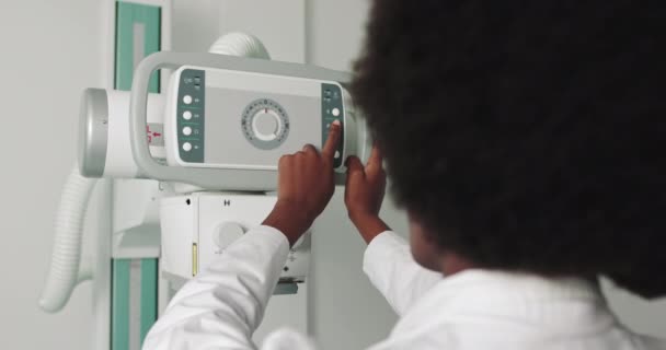 Portret profesjonalnego lekarza pochodzenia afrykańskiego uśmiechniętego do kamery. W szpitalu, technik dostosowuje skaner rentgenowski. Nowoczesny szpital z zaawansowanym technologicznie sprzętem medycznym — Wideo stockowe