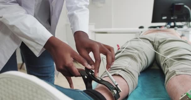 Doktor elektrokardiyogram yaptı ve enayileri çıkardı. Doktor elektrokardiyografiden önce insan bacaklarına elektrot koydu. İnsanın Elektrokardiyografisi. Afrikalı Amerikalı Doktor EKG yaptı. — Stok video