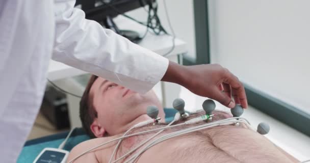 Krankenschwester befestigt Elektroden an den Gliedmaßen des Patienten für kardiologische Tests, Ausrüstung. Kardiologe verbindet den Patienten mit dem EKG-Gerät. Kardiologe bereitet sich auf Herz-Kardiogramm vor — Stockvideo