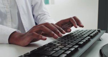 Hastanede klavyeye yazı yazan, tıbbi üniformalı Afrikalı genç bir kadının ellerini yakın çekim. Masada oturup bilgisayarla uğraşan güzel bir bayan hemşire. Teknoloji, sağlık, tıp konsepti.