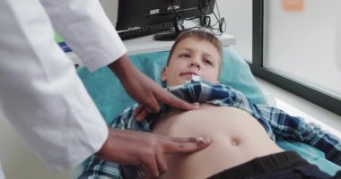 Afrikalı Amerikalı kadın doktor ya da çocuk doktoru. Akut Apandisit, Crohns Hastalığı ya da İltihaplı Bağırsak Hastalığı. Laparoskopik için Cerrahi Muayene ve Hazırlık. Genç bir erkek çocuk acı çekiyor.