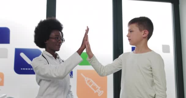 Професійний жіночий сімейний лікар-педіатр, який пояснює, як лікувати здоров'я, розмовляючи з милим хлопчиком дошкільного віку, пацієнт дає високу п'ятірку за концепцією дитячого огляду — стокове відео
