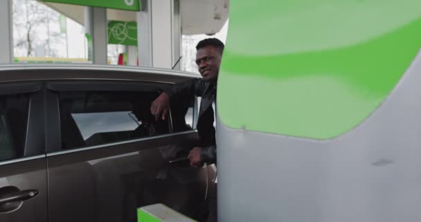 Benzin istasyonunda elinde kahve olan Afrikalı bir adamın portresi. Seyahat ederken arabaya yakıt doldurmak, benzin istasyonunda durmak, kahve içmek. Yakıt, benzin istasyonu, benzin fiyatları kavramı — Stok video