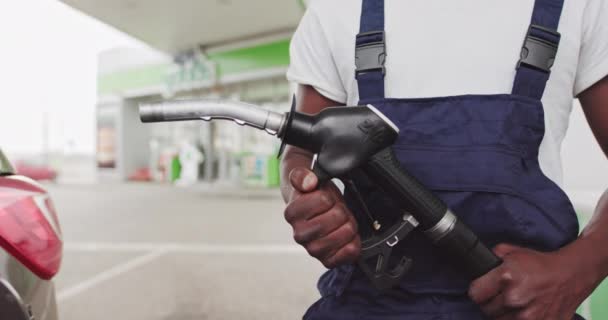 Un trabajador africano de reabastecimiento de combustible negro sostiene un arma para realimentar un automóvil. Primer plano de un arma en las manos de un trabajador negro. Gasolina, Gas, Gasolina, Combustible, Concepto de Petróleo. — Vídeos de Stock