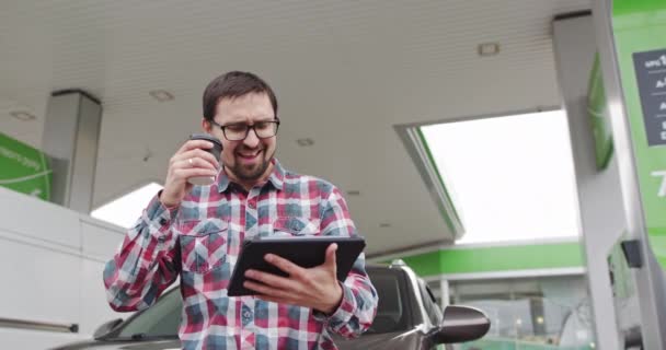 Close up of happy handsome man in glassess looking to tablet and smiling. Bearded male office worker in good mood. People portraits. Man Standing Near His Car While He Refuels At A Gas Or Diesel — Stock Video