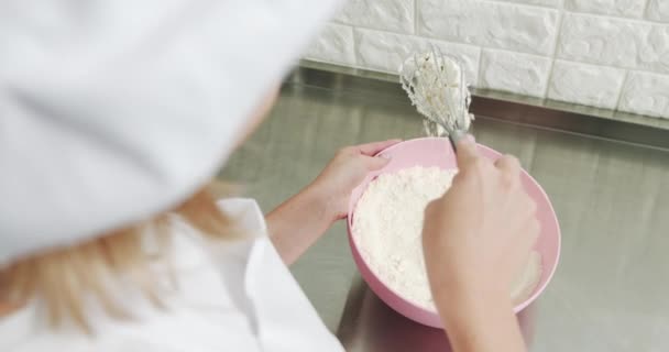 Pasticciere donna, indossando cappello e grembiule, mescolando la farina in una ciotola rosa con un frullato. Preparazione per la fabbricazione di macaron nel laboratorio di panetteria. Impastare la farina a mano. Cottura professionale — Video Stock