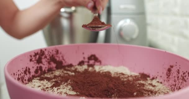 Donna primo piano aggiungendo cacao alla ciotola per cucinare il cioccolato fatto in casa. Donna Pasticcere, con cappello bianco e grembiule, versando cacao in polvere nella ciotola. Preparazione di maccheroni, torte e dessert — Video Stock