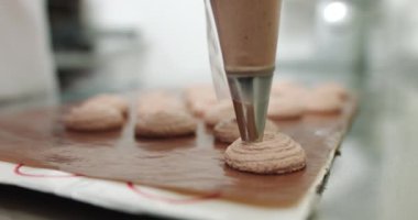 Şef makaron tatlısı hazırlamak için zemin hazırlıyor. Makaron tatlısı pişirmek için metal tepside bulunan boru torbasından çıkan kas kreminin yakın çekimi..