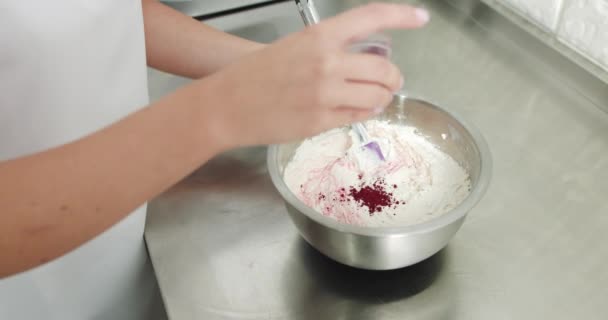 Nahaufnahme einer weiblichen Konditorin, die Sahne für Kuchen oder Plätzchen-Macarons macht, Zutaten in der Schüssel mischt und Lebensmittelfärbepulver hinzufügt, um die Farbe zu ändern. Blick von hinten — Stockvideo