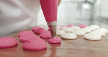 Arka tepsideki mindere pembe badem kurabiyesi karışımı dökmek, şefin boru torbasından makarna yapması. Genç bir kadın pastacı, sıcak pastanesinde makaron yapıyor. Pembe makaronlar yapıyorum..