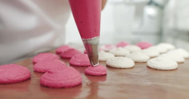 Tăierea amestecului de macaroane roz pe un covor de alunecare pe tava de susținere, bucătar care face macaroane cu sac de conducte. Femeie tânără cofetar face macaroane în magazinul ei confortabil de patiserie ușoară. Efectuarea macaronilor roz . — Videoclip de stoc