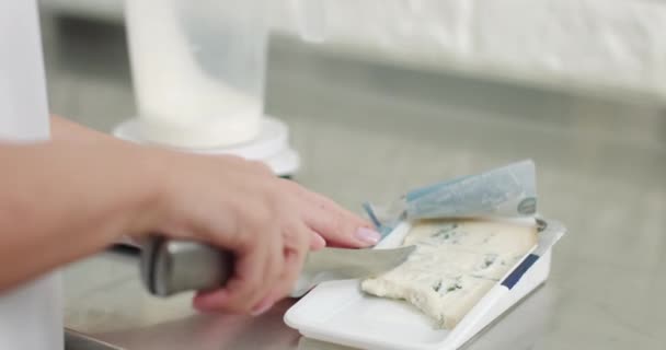 Cerrar imagen recortada de las manos de la hembra pastelera en delantal blanco, cortado con un cuchillo sabroso queso gorgonzola. Queso en proceso de cocción. Chef rebanando queso cottage — Vídeos de Stock