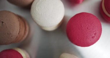 Beyaz Arkaplan Beyaz Pembe ve Kahverengi Macaron üzerine renkli Pastel Makarnalar. Açık mutfak veya şekerci dükkanının masasındaki renkli beyaz, kırmızı ve karamel çikolatalı makarna tatlılarını yakın.