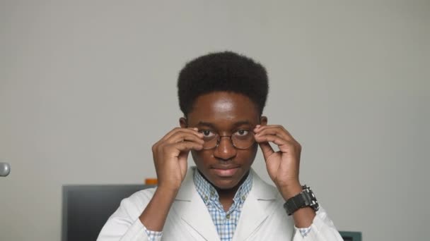 Close Up Portrait of African American Family Medical Doctor in Glasses is in Health Clinic. Successful Black Physician in White Lab Coat Looks at the Camera and Smiles in Hospital Office. — Stock Video