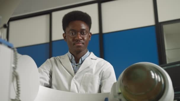 Нижній погляд на молодого впевненого африканського лікаря в білій формі, який працює з сучасним обладнанням для лікування ниркових каменів. Неінвазивна екстракорпоральна літотріпсія ударних хвиль — стокове відео