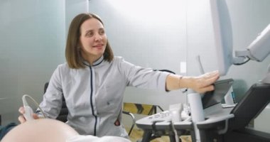 Doğum kliniğinde ultrason taraması sırasında hamile bir kadının görüntüsü alındı. Kadın doktor ultrason makinesini işaret ediyor. Hamile karnındaki ultrason dönüştürücüsüne odaklan.