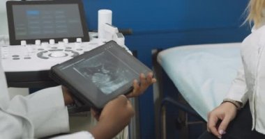Kanepede oturan hamile bir kadına bebek ultrason görüntüsüyle dijital tablet gösteren Afrikalı bir erkek doktorun kesilmiş görüntüsünü kapat. Tablete odaklan.