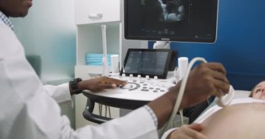 Erkek Afrikalı doktorun ellerini yakın çekim, ultrason dönüştürücü ile hamile karnını tarama, kontrol panelindeki düğmelere basma. Elindeki düğmelere odaklan.