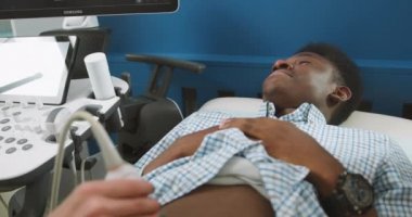 Ultrason tarayıcısının yakın görüntüsü, profesyonel bir kadın doktorun elinde. Genç Afrikalı hastayı muayene ediyor, ultrason taraması yapıyor.