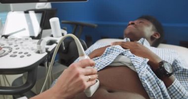 Ultrason tarayıcısının yakın görüntüsü, profesyonel bir kadın doktorun elinde. Genç Afrikalı hastayı muayene ediyor, ultrason taraması yapıyor.