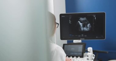 Modern ultrason cihazları üzerinde çalışan beyaz kadın doktor. Ultrason tarama makinesi operatörü oturuyor ve ekrana bakıyor, iş için hazırlanıyor.