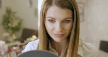 Genç bir kadın aynaya bakar, kendini hazırlar, kendine hayran olur, kıyafetlerini ve saç stilini düzeltir. Gülümsüyor ve kendini seviyor. Yeni bir güne başla. Sabahın tadını çıkar. Güzellik salonu makyajı.