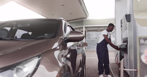 Junge, gut aussehende afrikanische männliche Arbeiter an der Tankstelle betanken das Auto ihrer Kunden mit Benzin. Übersetzt: ENERGIE IHRER BEWEGUNG — Stockvideo