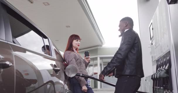 Un par en la gasolinera. Feliz alegre pareja multirracial de amigos o colegas, posando ante la cámara, divirtiéndose mientras repostan autos de lujo en la gasolinera, dándose chocos y sonriendo — Vídeos de Stock