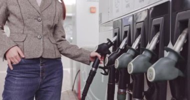 Moda kıyafetleri içinde beyaz bir iş kadınının portresi. Benzin istasyonunun pompa panelinden doldurma başlığını alıyor.