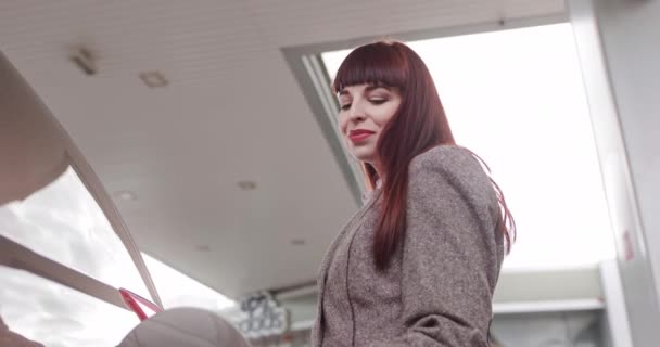Jeune jolie femme aux cheveux rouges caucasienne en tenue décontractée tendance, rechargeant de l'essence dans sa voiture moderne de luxe à la station-service libre-service — Video