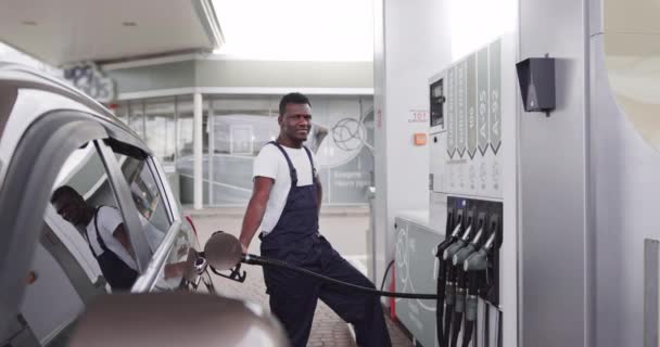 Jonge knappe Afrikaanse mannelijke werknemer bij tankstation tanken klanten auto met benzine. Vertaling: ENERGIE MOVEMENT — Stockvideo