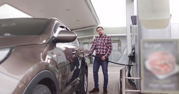 Čerpací stanice, koncepce automatického tankování. Portrét mladého pohledného bělocha stojícího venku na benzínce a tankujícího luxusní auto benzínem. Překlad: ENERGY MOVEMENT — Stock video