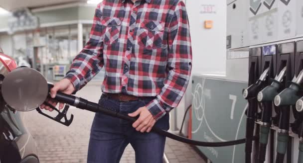 Primer plano retrato de joven guapo hombre caucásico, con ropa casual elegante, repostando su coche de lujo en la gasolinera al aire libre. Reabastecimiento del concepto de automóvil — Vídeo de stock