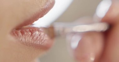 Makyaj sanatçısı ruj sürüyor. Genç bir kadının dudaklarına yakın plan, profesyonel makyaj sanatçısı fırçayla doğal renkte ruj sürmüş. Kuliste moda. Güzellik salonu. Pembe arkaplan