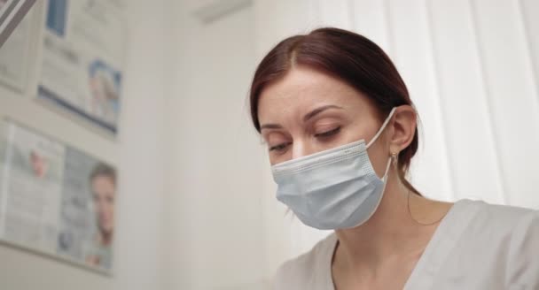 Κοντινό πρόσωπο μιας γιατρού με προστατευτική μάσκα, μια ιατρική μάσκα. Γιατρός κατά τη διάρκεια της εργασίας. Ερευνητής. Ο γιατρός ή η νοσοκόμα φοράει μάσκα υγιεινής στο χώρο εργασίας. Έννοια κλινικής ομορφιάς. — Αρχείο Βίντεο