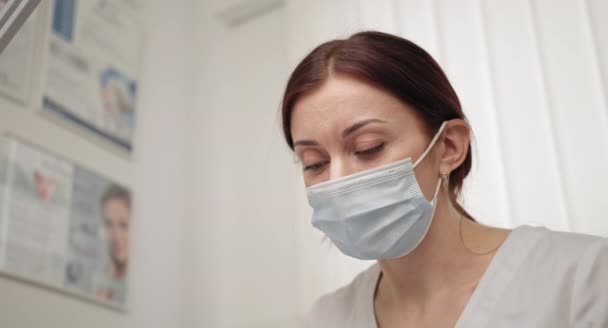 Viso ravvicinato di una dottoressa con una maschera protettiva, una maschera medica. Medico durante il lavoro. Ricercatore. Dottore o infermiera indossa una maschera igienica sul posto di lavoro. Concetto di clinica estetica. — Video Stock