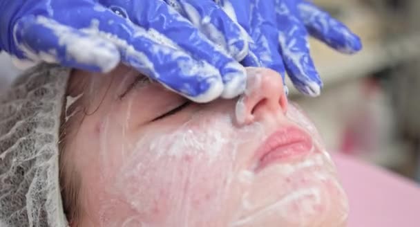 O médico esteticista está aplicando espuma de limpeza facial no rosto das mulheres massageando a pele na clínica de cosmetologia. Cosmetologist que faz o procedimento do cuidado da pele no salão de beleza, retrato da mulher nova, vista superior. — Vídeo de Stock