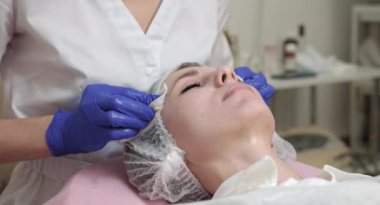 Mükemmel profesyonel cilt temizliği, spa tedavisi, yüz bakımı. Mavi eldivenli kadın doktor elleri süngerle güzel bir kadının tenini temizliyor..