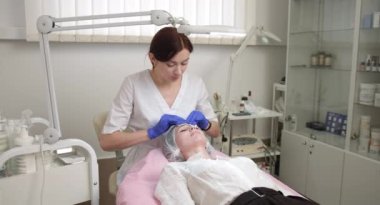 Güzel bir kadının tenini süngerle temizlemek. Mükemmel profesyonel cilt temizliği, spa tedavisi, yüz bakımı. Mavi eldivenli kadın doktor elleri.