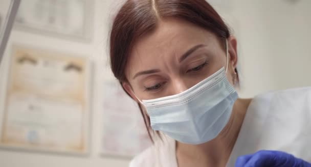 Face de perto de uma doutora numa máscara protectora, uma máscara médica. Médico durante o trabalho. Pesquisador. Médico ou enfermeiro está usando máscara de higiene no local de trabalho. Conceito de clínica — Vídeo de Stock