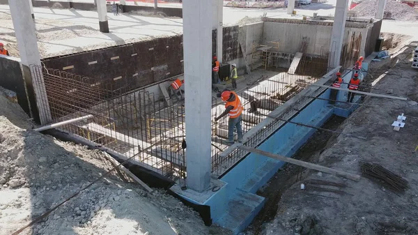 Volo aereo su un sito di sviluppo di nuove costruzioni con diversi team di ingegneri e architetti. I lavoratori lavorano in cantiere strutture in cemento armato. Costruzione monolitica moderna — Foto Stock