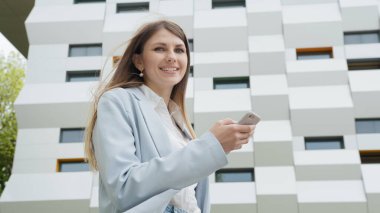 İş kadını akıllı telefon mesajları kullanıyor kadın yönetici e-postaları kontrol ediyor. İş için. Sosyal ağ. Uygulamalar. Kariyer insanları. Ofisin yakınındaki sokakta ateş edildi. Kız kameraya bakar ve gülümser.