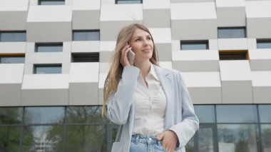 Beyaz Gömlekli Beyaz Kendinden emin genç İş Kadını Modern Ofis Binası 'nın yakınında telefonda konuşuyor. Orta Uzun Düşük Açı 4K Yavaş Hareket Şirketi Hareketli Çekim. Kariyer insanları