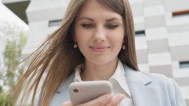 Sosyal medya uygulamasını akıllı telefon mesajlarında kullanan zarif genç bir bayana açık havada gülümseyen haberler geliyor. İnsan portreleri. Teknoloji. Kapalı kapılar ardında neşeli bir kız telefonda iyi haberler okuyor..